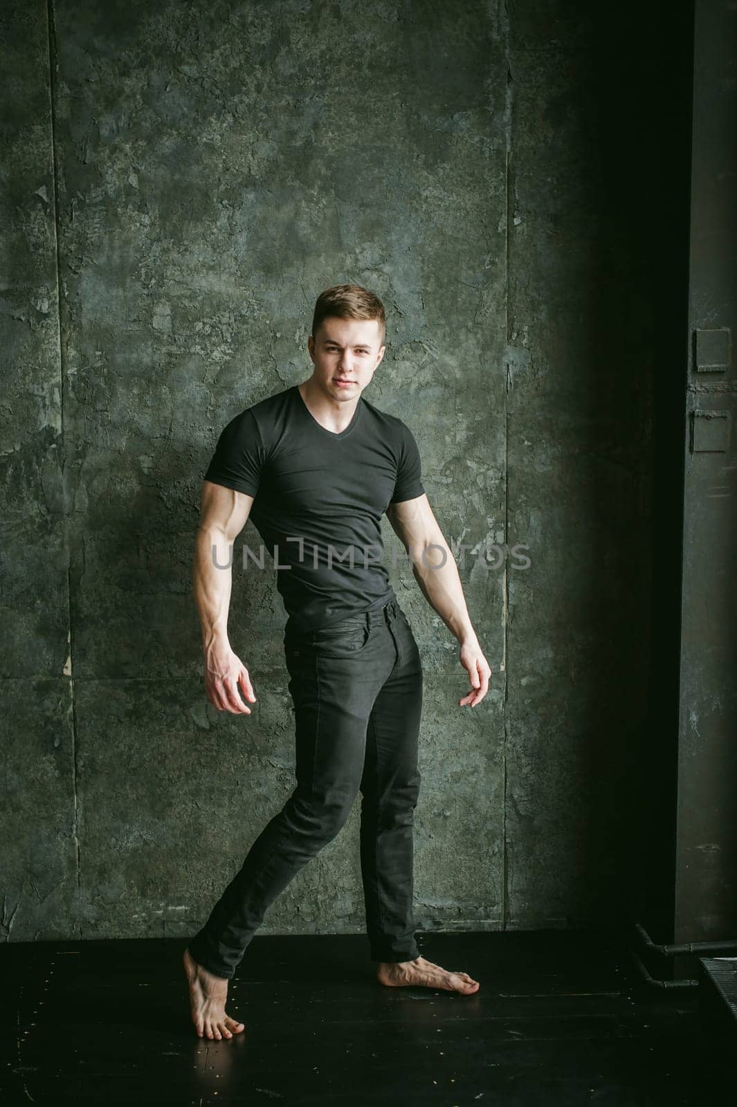 Young sexy men bodybuilder athlete, studio portrait loft on background of stylized Concrete brutal wall, guy model black Tshirt and trousers
