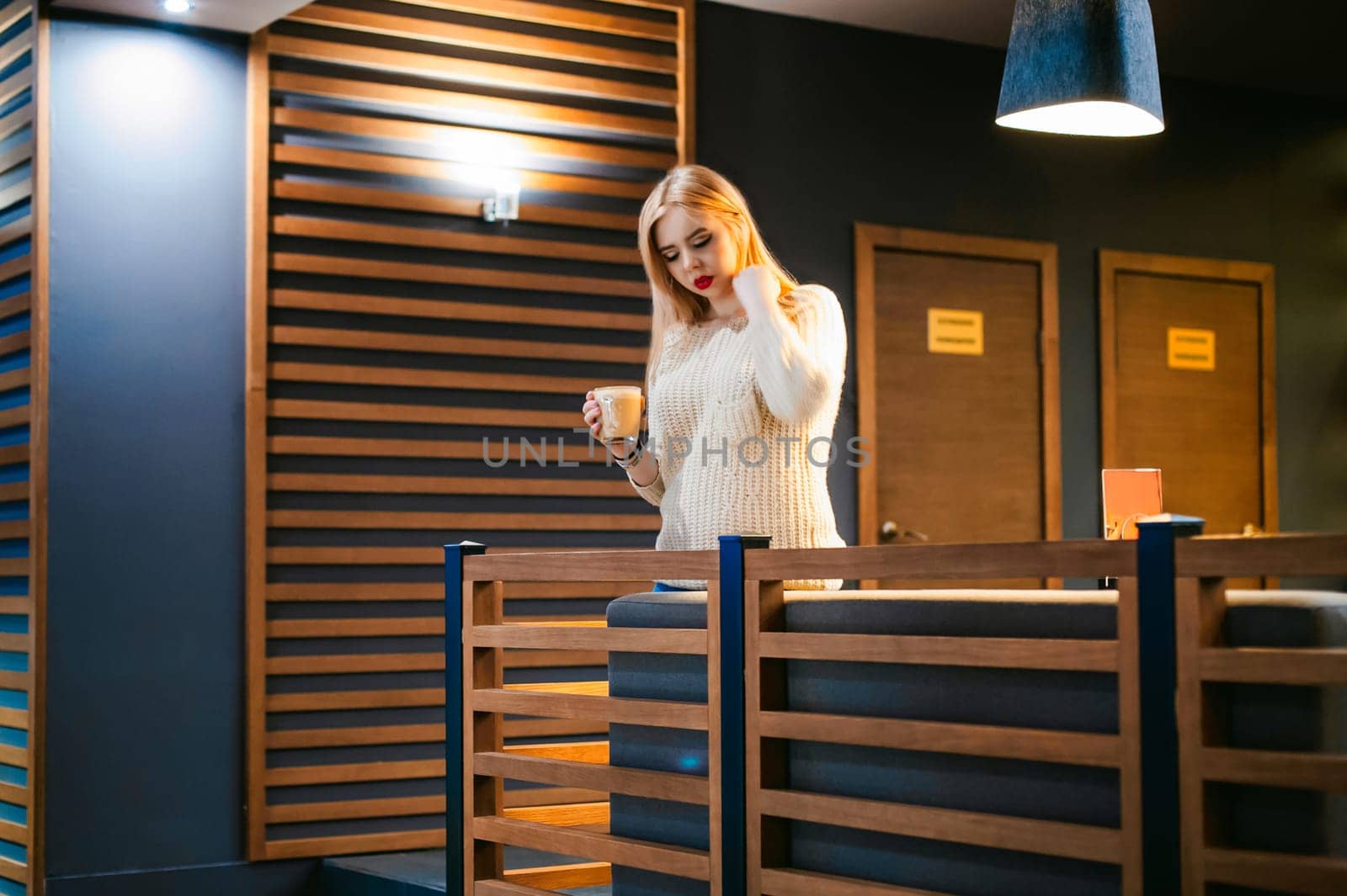 Cute young blonde woman drinks hot coffee from a glass cup in the interior of a coffee house