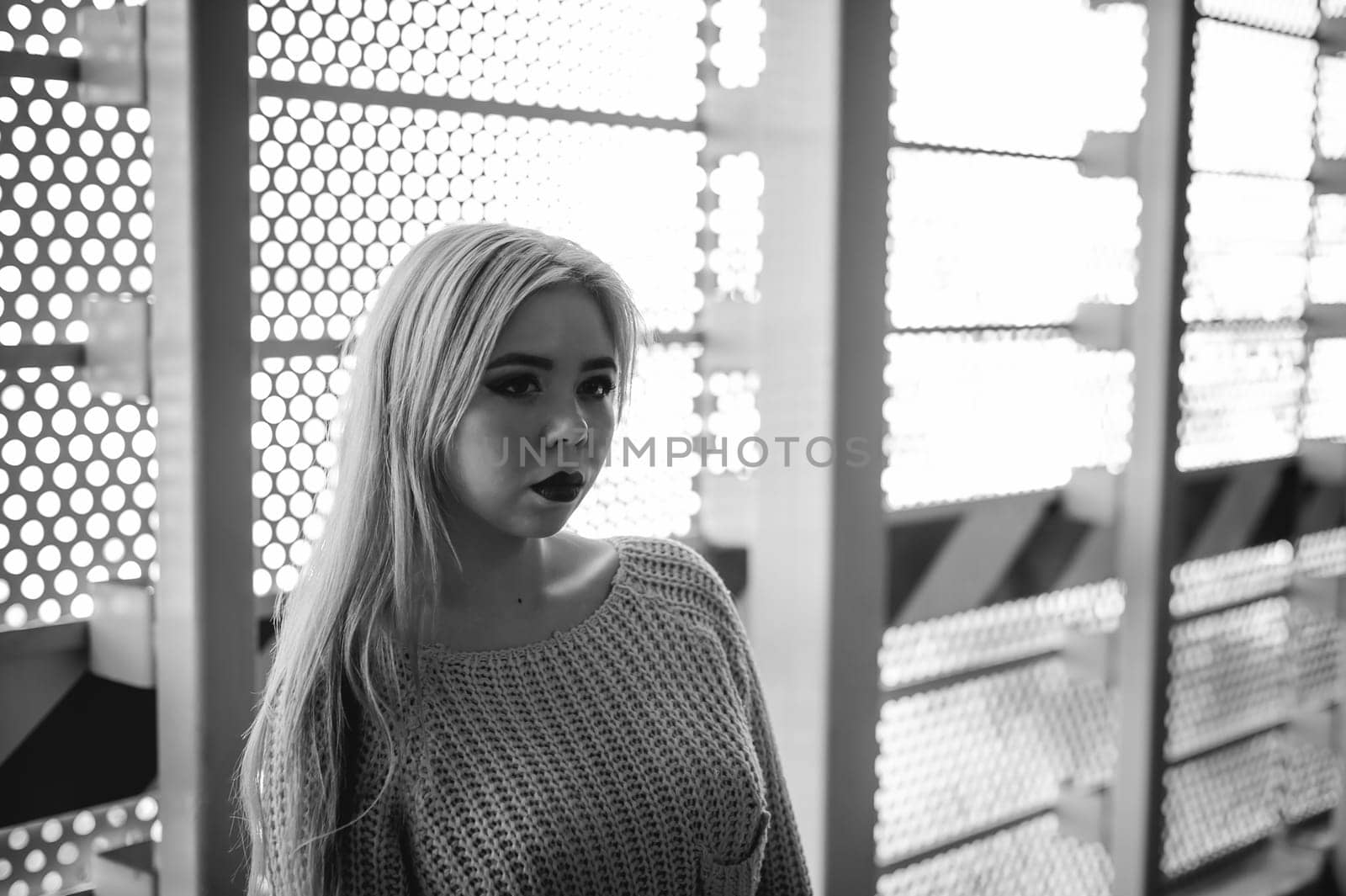 Portrait of a young woman dressed in a knitted sweater and blue jeans. Standing near a metal perforated parking fence construction
