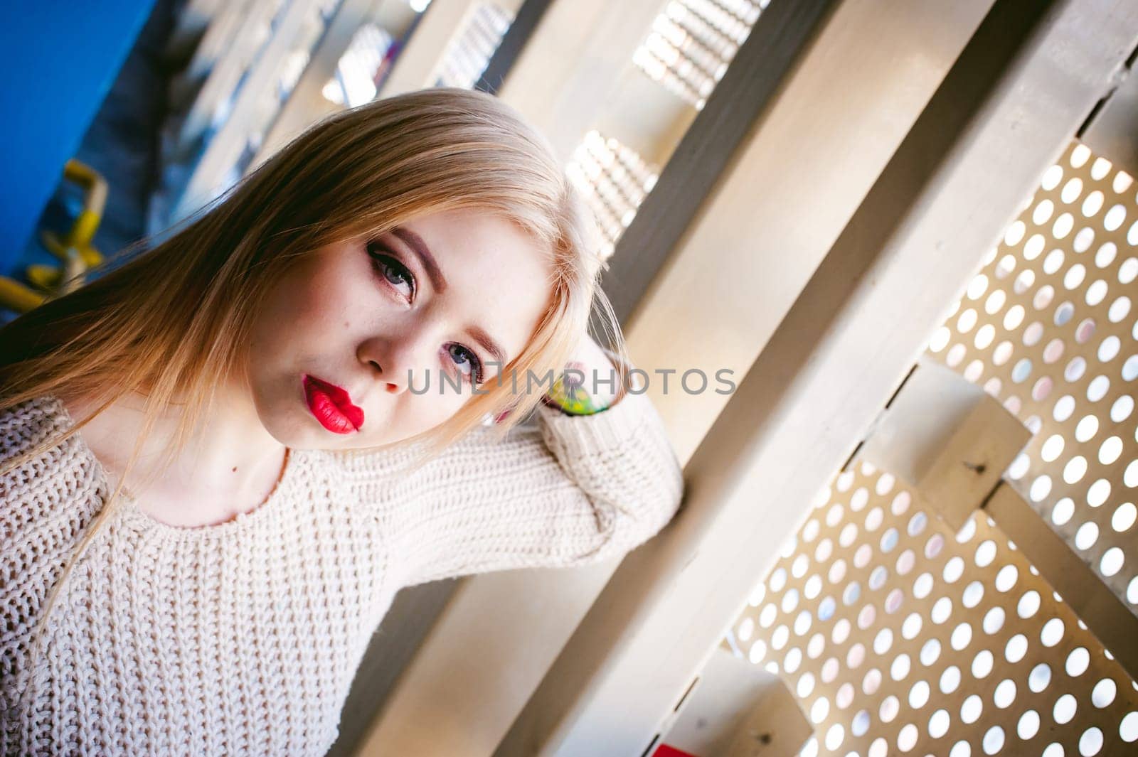 Portrait of a young woman dressed in a knitted sweater and blue jeans. Standing near a metal perforated parking fence construction
