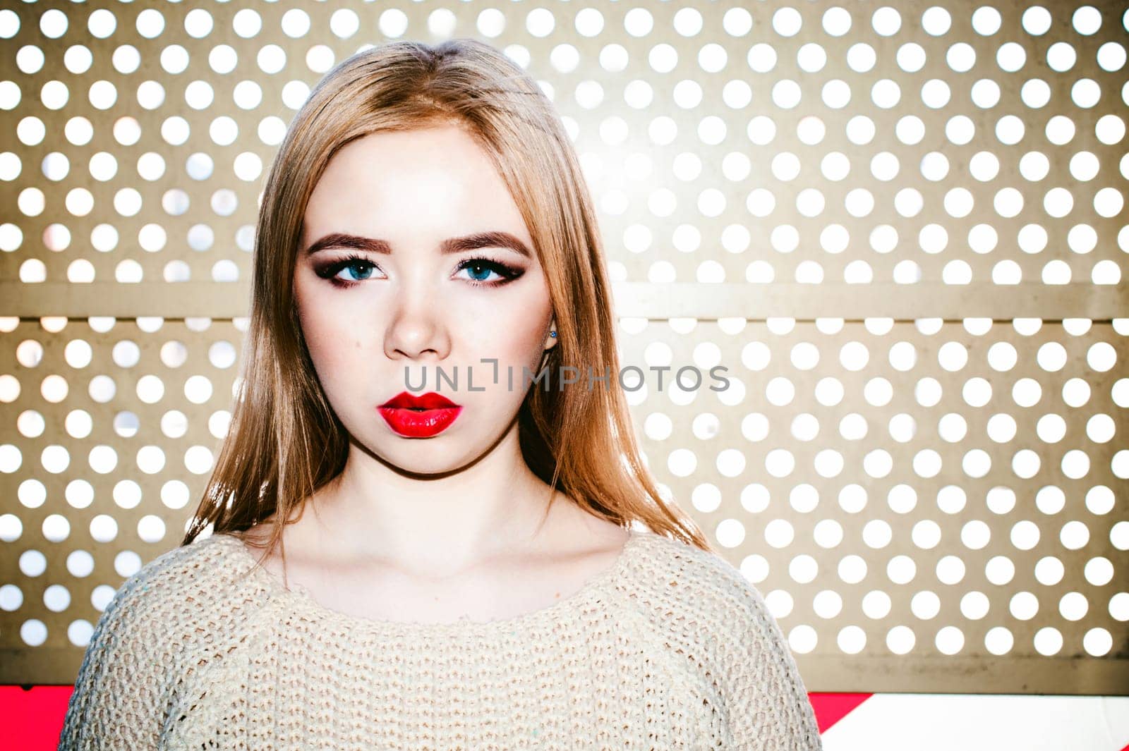Portrait of a young woman dressed in a knitted sweater and blue jeans. Standing near a metal perforated parking fence construction