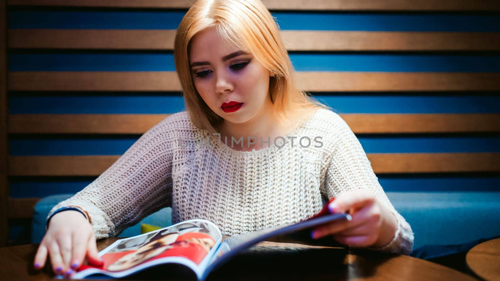 Picture of young lady sitting in cafe while reading magazine.