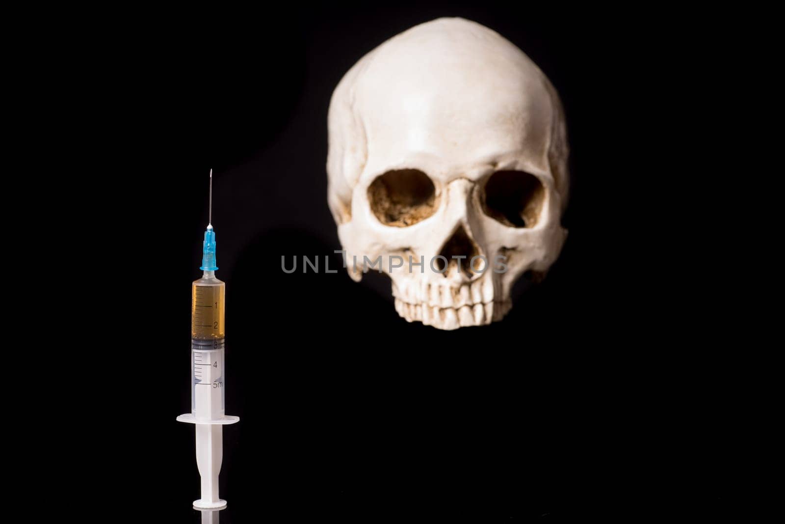 Syringe with brown liquid and blurry skull isolated on black background