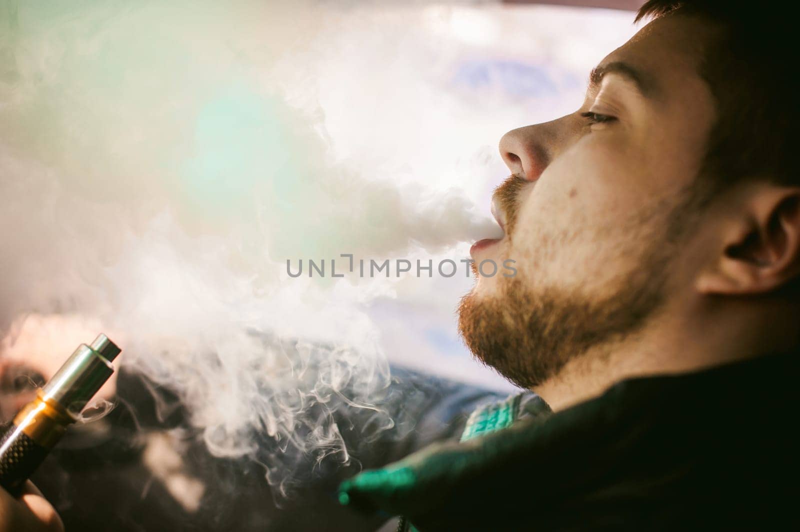 young vaper man with beard vaping mechanical mod. Guy smokes an electronic cigarette by blowing a smoke vapor