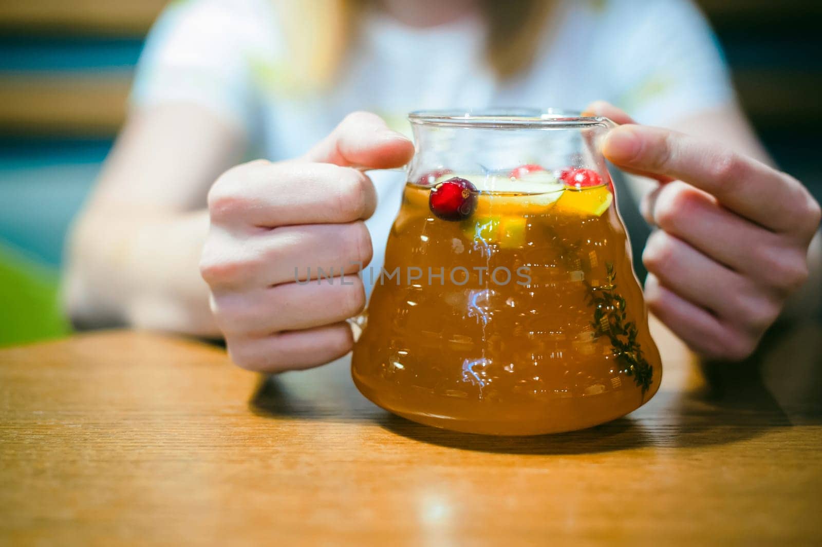 Young blonde woman wearing white T-shirt with print, girl Holds a glass jug in his hand, sitting at a table in a cafe, background stylized Wood texture lit up with warm light