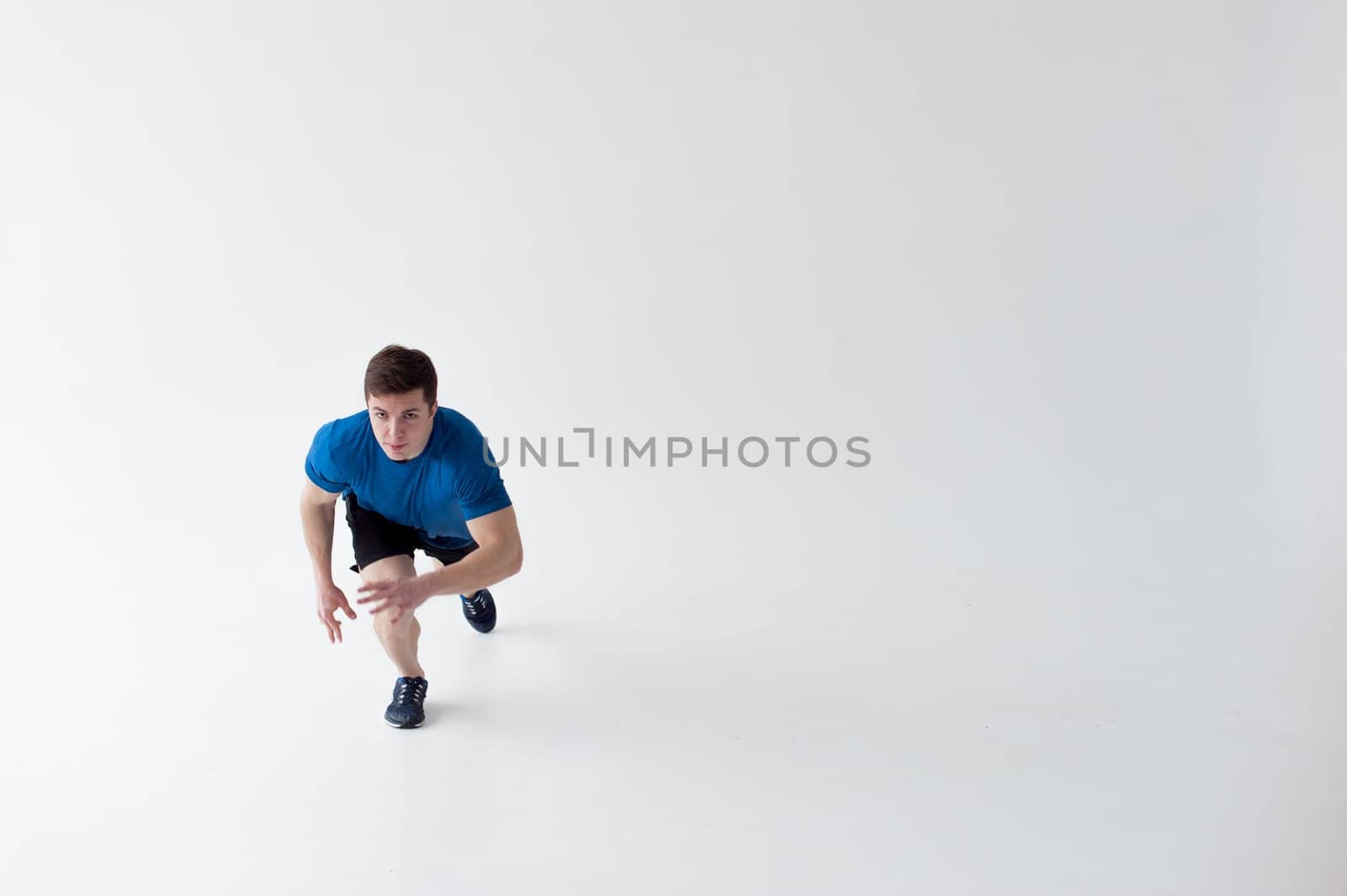 Running man on low start. Stands in rack, ready to achieve goals and wins. Young sexy Muscular male athlete wearing sporty blue t-shirt and shorts, studio portrait white background.Motivation concept