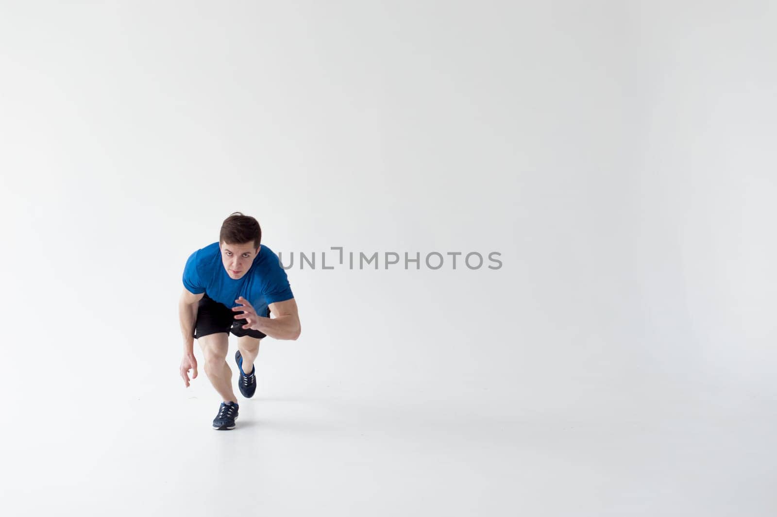 Running man on low start. Stands in rack, ready to achieve goals and wins. Young sexy Muscular male athlete wearing sporty blue t-shirt and shorts, studio portrait white background.Motivation concept