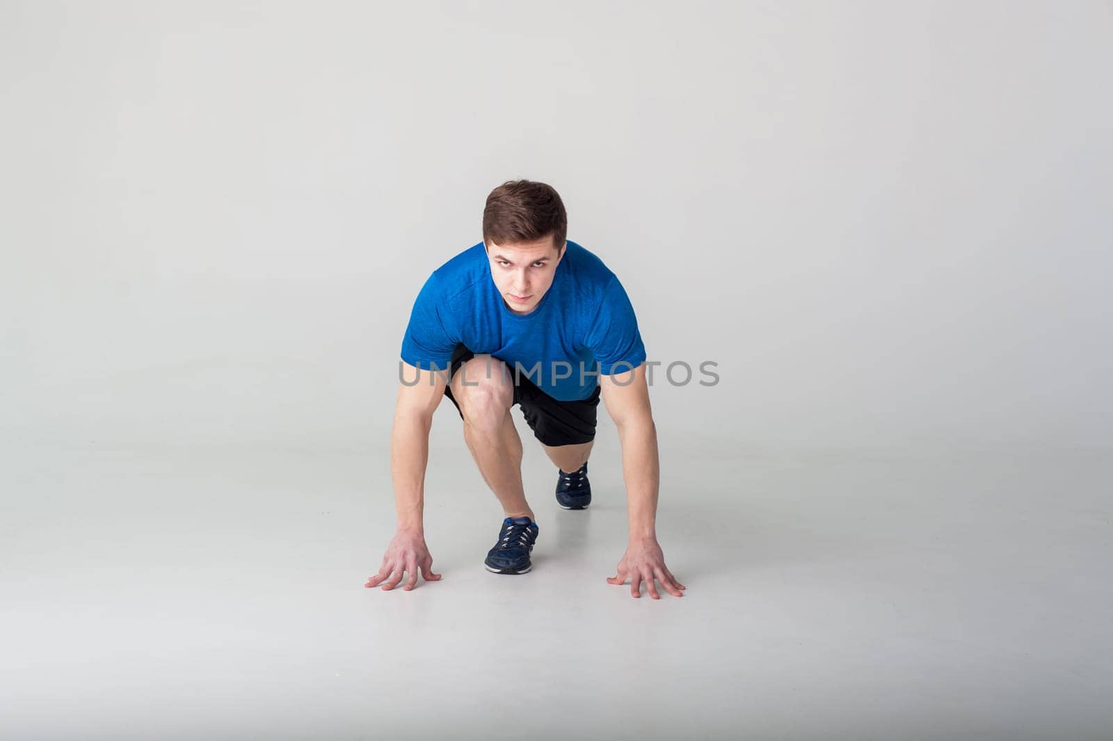 Running man on low start. Stands in rack, ready to achieve goals and wins. Young sexy Muscular male athlete wearing sporty blue t-shirt and shorts, studio portrait white background.Motivation concept