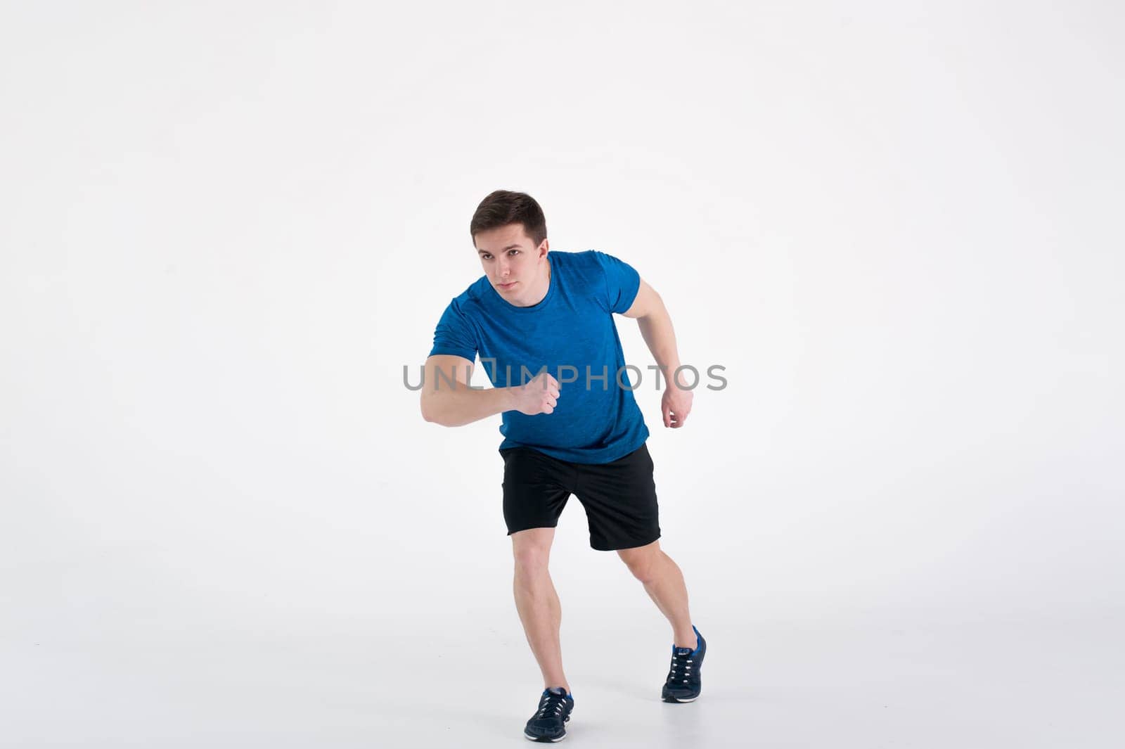 Running man on low start. Stands in rack, ready to achieve goals and wins. Young sexy Muscular male athlete wearing sporty blue t-shirt and shorts, studio portrait white background.Motivation concept