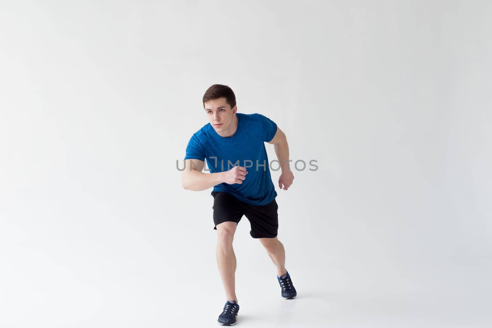 Running man on low start. Stands in rack, ready to achieve goals and wins. Young sexy Muscular male athlete wearing sporty blue t-shirt and shorts, studio portrait white background.Motivation concept