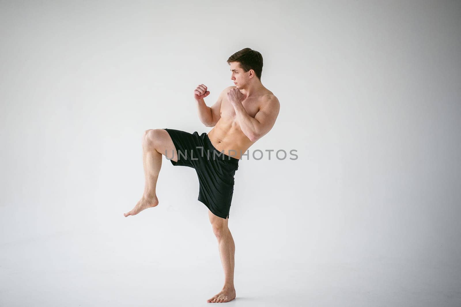 young sexy handsome men strong Athlete's body with bare torso, Dressed black sports shorts, portrait of studio of light-skinned strong man standing in fighting stance Kicking, straining powerful legs