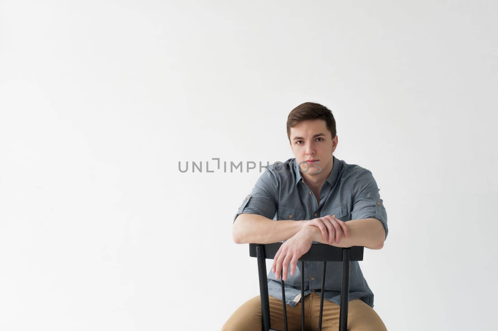 Man dressed in a shirt and brown trousers sits on a wooden vintage chair on a white background