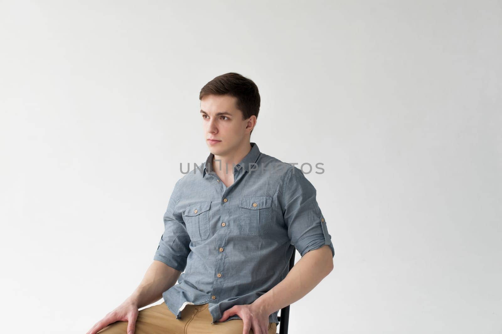 Man dressed in a shirt and brown trousers sits on a wooden vintage chair on a white background