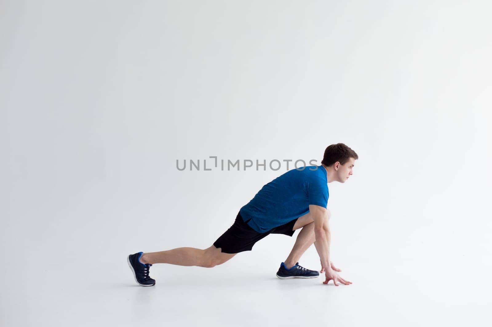 Running man on low start. Stands in rack, ready to achieve goals and wins. Young sexy Muscular male athlete wearing sporty blue t-shirt and shorts, studio portrait white background.Motivation concept