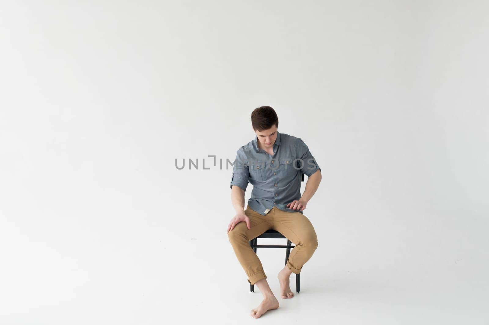 Man dressed in a shirt and brown trousers sits on a wooden vintage chair on a white background