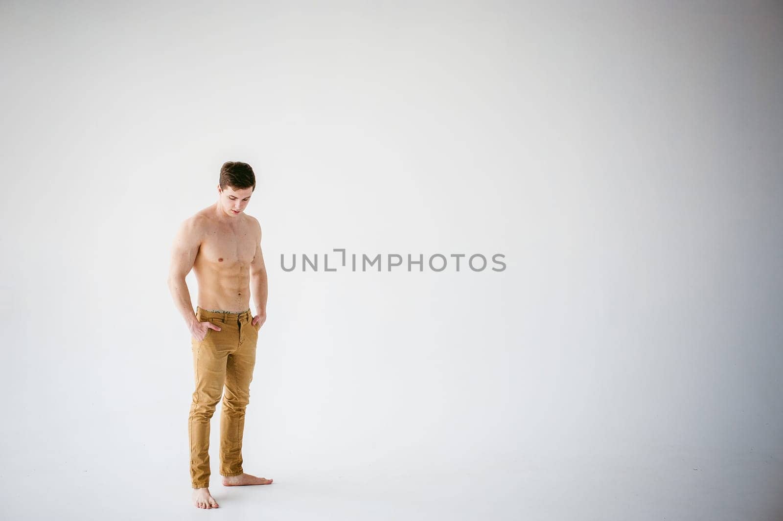 portrait young sexy handsome man of strong Athlete's body with bare torso, Dressed  brown trousers, Posing on white studio background