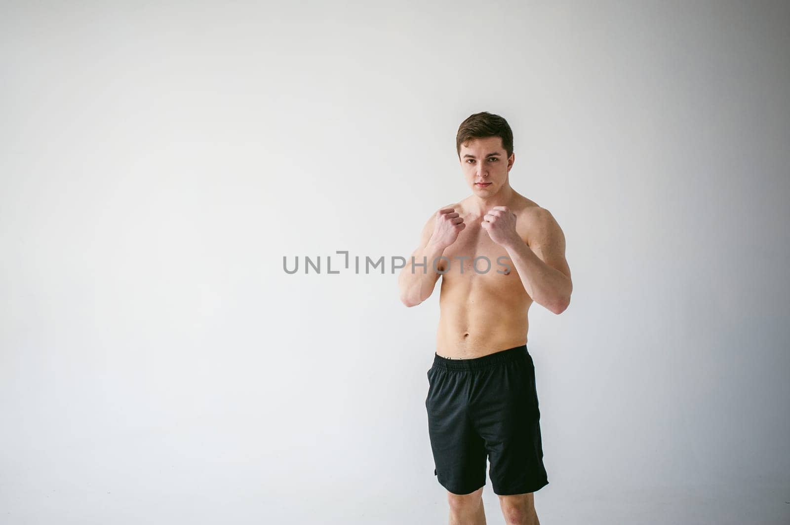 young sexy handsome men of strong Athlete's body with bare torso, Dressed black sports shorts, portrait of studio of light-skinned strong man standing in fighting stance, straining powerful hands