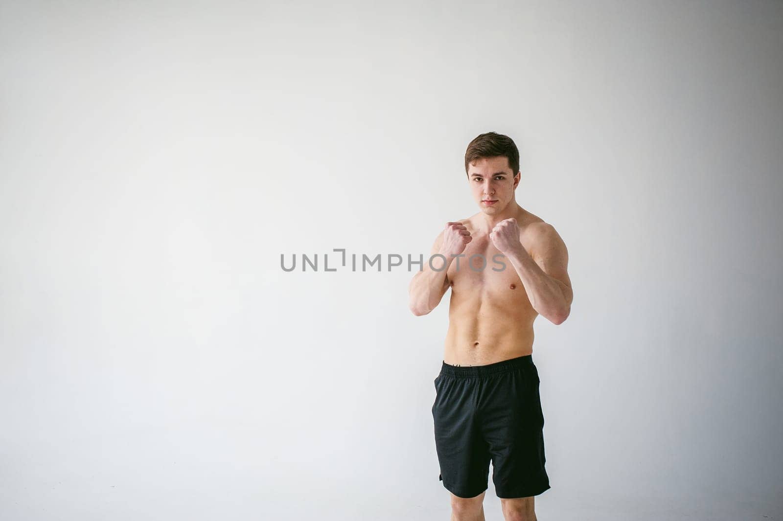 young sexy handsome men of strong Athlete's body with bare torso, Dressed black sports shorts, portrait of studio of light-skinned strong man standing in fighting stance, straining powerful hands