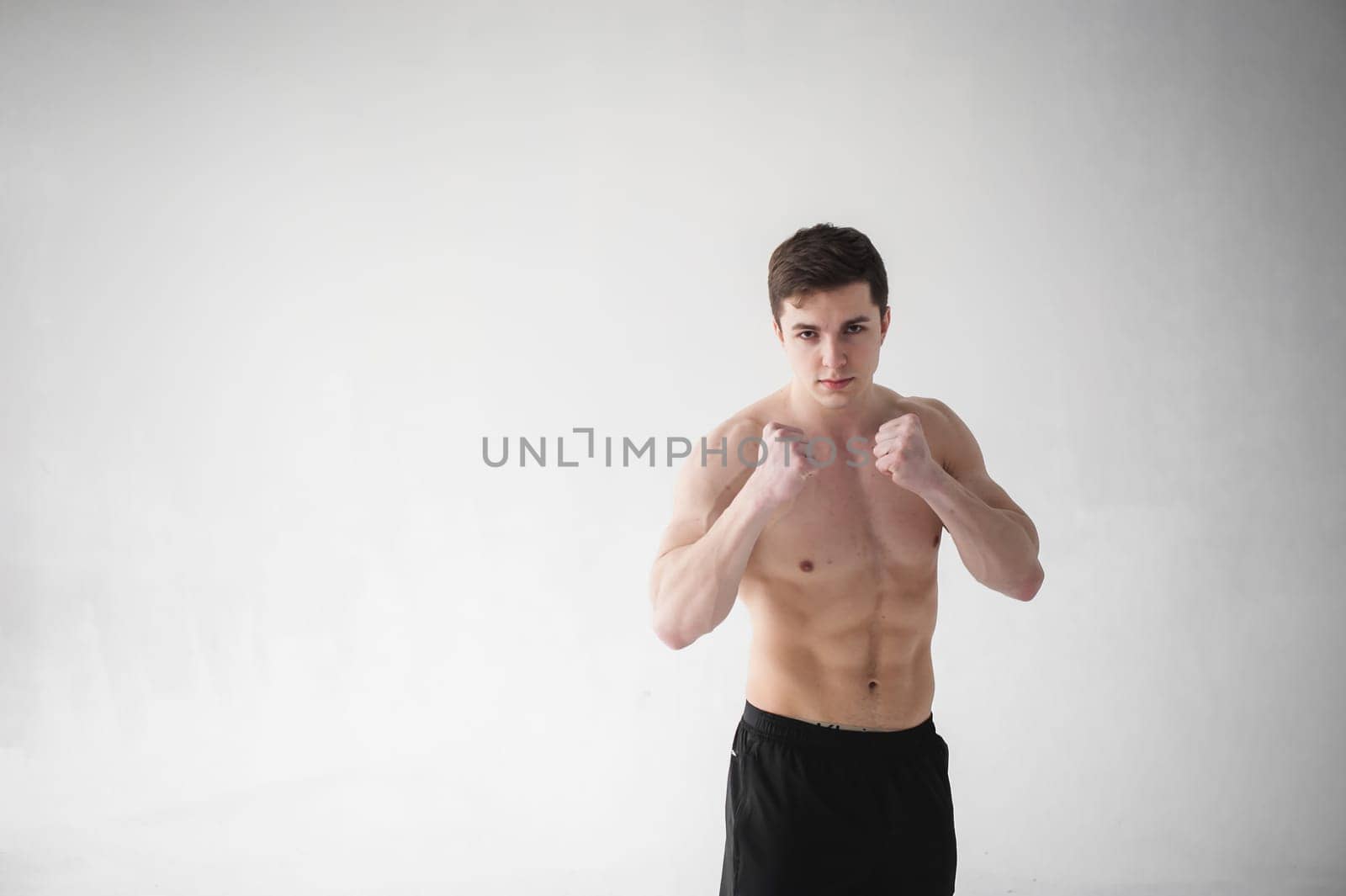 young sexy handsome men of strong Athlete's body with bare torso, Dressed black sports shorts, portrait of studio of light-skinned strong man standing in fighting stance, straining powerful hands