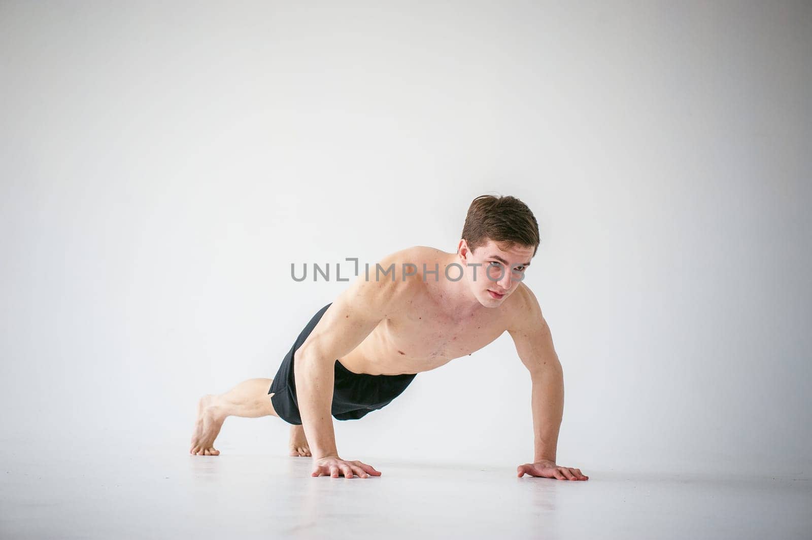 young sexy handsome men of strong Athlete's body with bare torso, Dressed black sports shorts, portrait of studio of light-skinned strong man engaged in push-ups, on floor, straining powerful hands