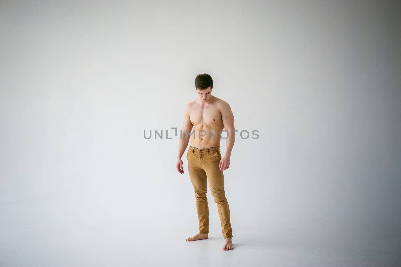 portrait young sexy handsome man of strong Athlete's body with bare torso, Dressed  brown trousers, Posing on white studio background