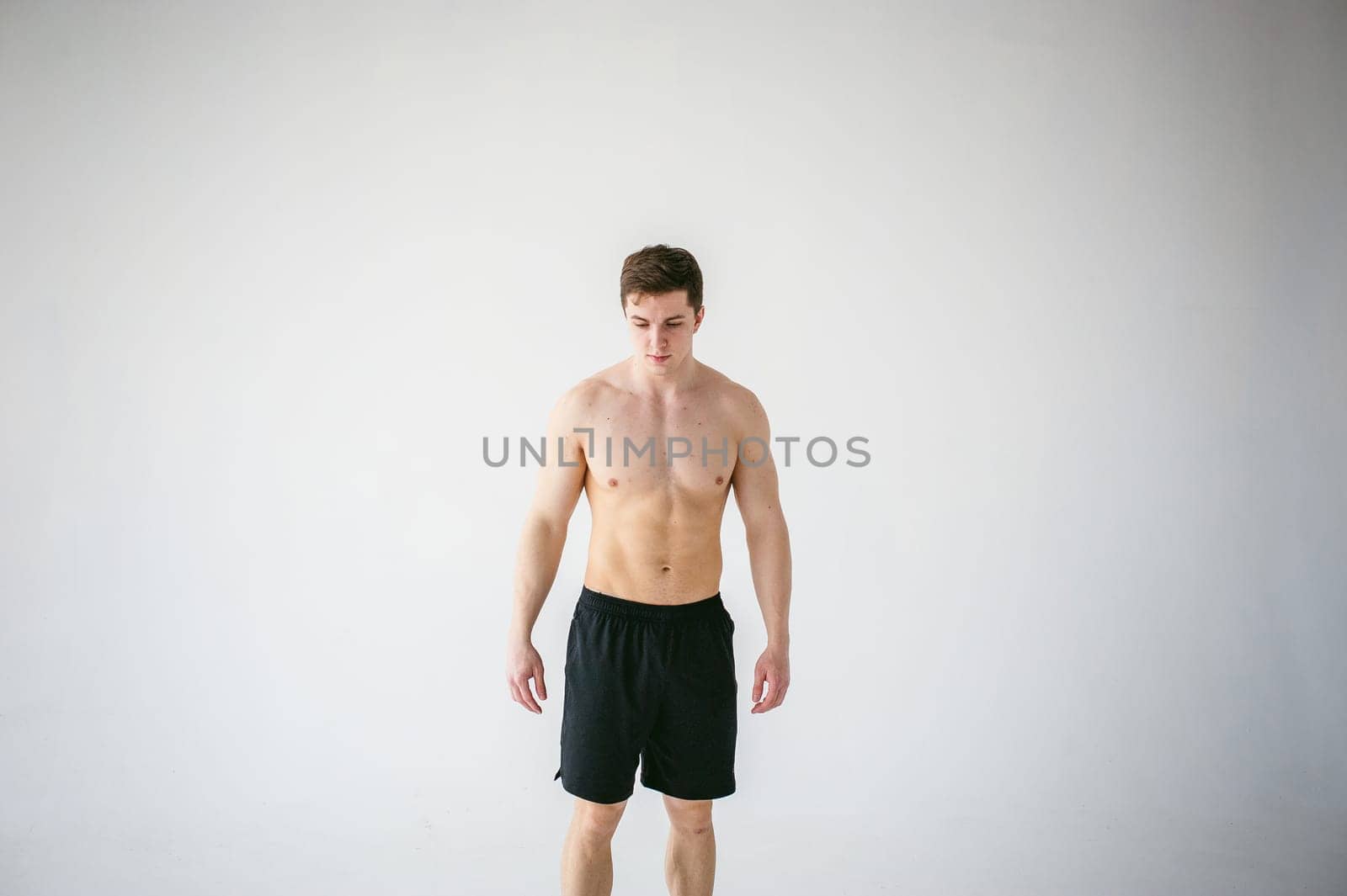 portrait young sexy handsome man of strong Athlete's body with bare torso, Dressed in a black sports shorts, Posing on white studio background