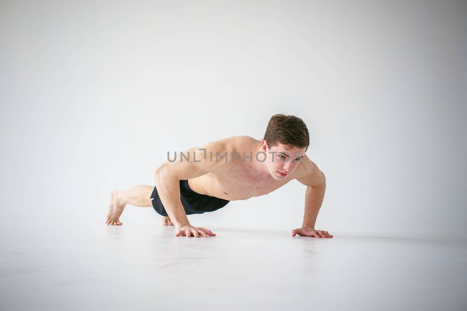 young sexy handsome men of strong Athlete's body with bare torso, Dressed black sports shorts, portrait of studio of light-skinned strong man engaged in push-ups, on floor, straining powerful hands