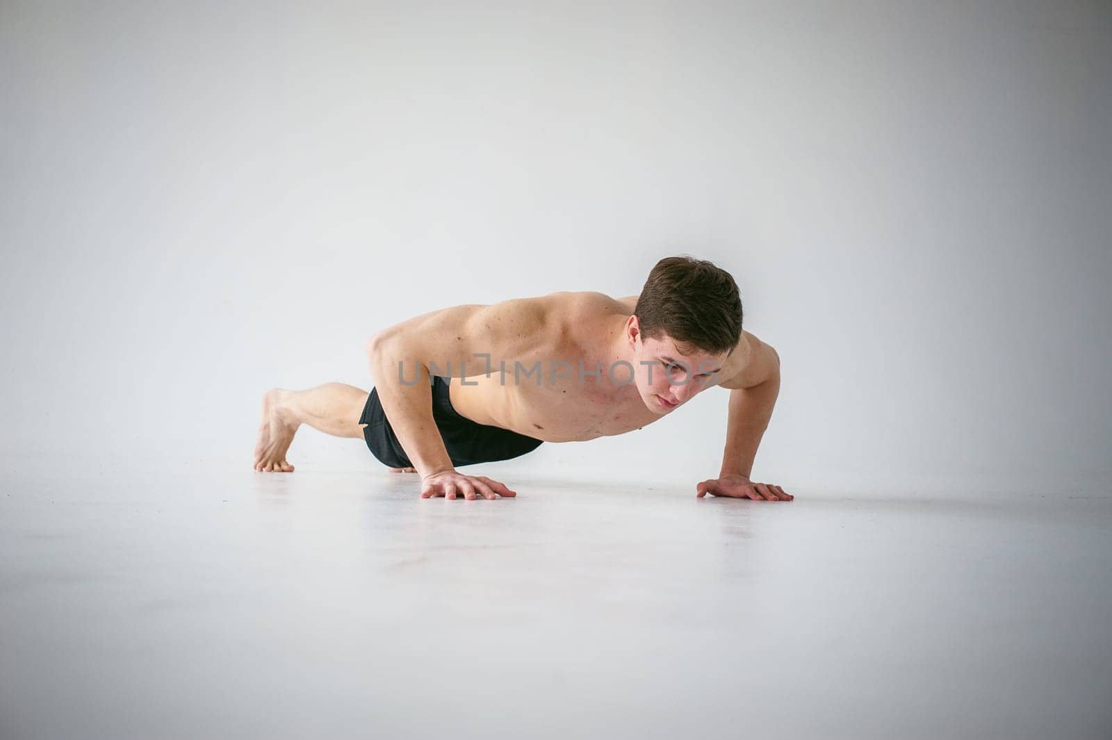 young sexy handsome men of strong Athlete's body with bare torso, Dressed black sports shorts, portrait of studio of light-skinned strong man engaged in push-ups, on floor, straining powerful hands