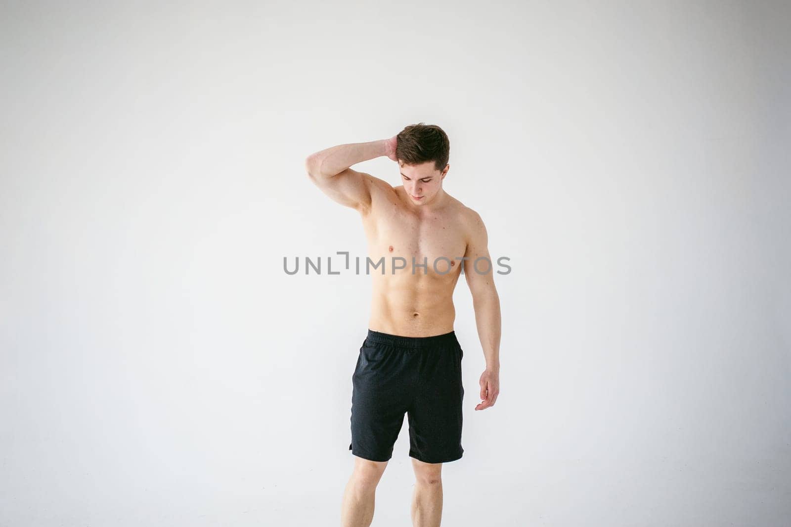portrait young sexy handsome man of strong Athlete's body with bare torso, Dressed in a black sports shorts, Posing on white studio background