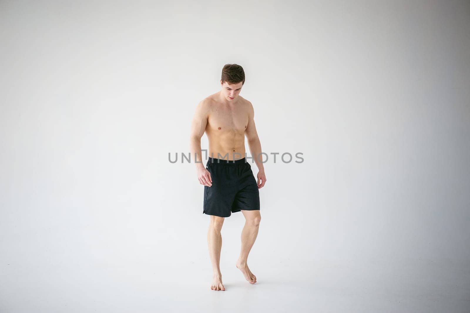 portrait young sexy handsome man of strong Athlete's body with bare torso, Dressed in a black sports shorts, Posing on white studio background
