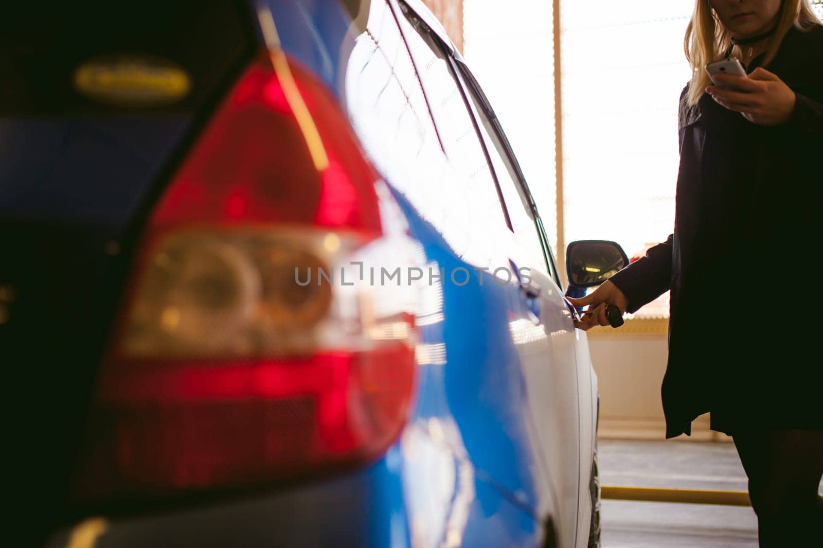 Woman in parking lot on blue car background. Opens door with key