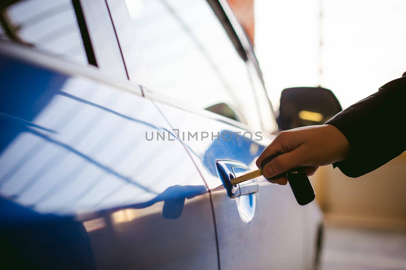 Woman in parking lot on blue car background. Opens door with key