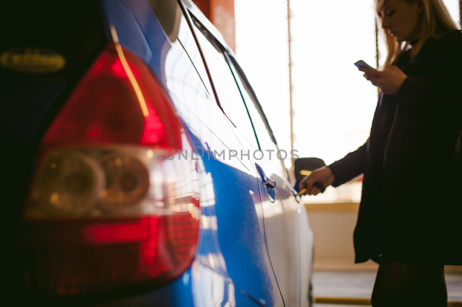 Woman in parking lot on blue car background. Opens door with key