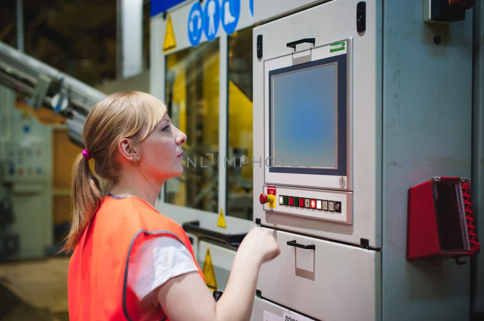 Portrait of a female employee in an orange robe vest in the working space of a production facility, supervises and controls the line in food production, against the background of equipment