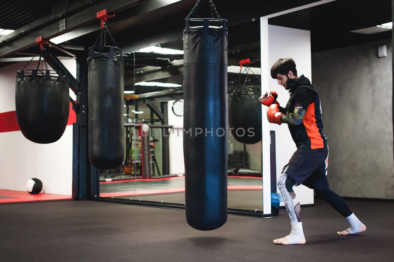 Professional Muay Thai fighter. Male boxer in training sportswear, an exercise in sports hall, Training with a punching bag, working out blows