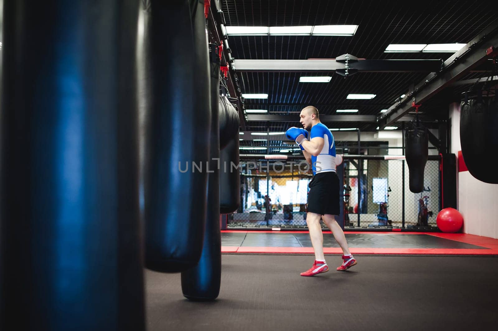 Professional Muay Thai fighter. Male boxer in training sportswear, an exercise in sports hall, Training with a punching bag, working out blows