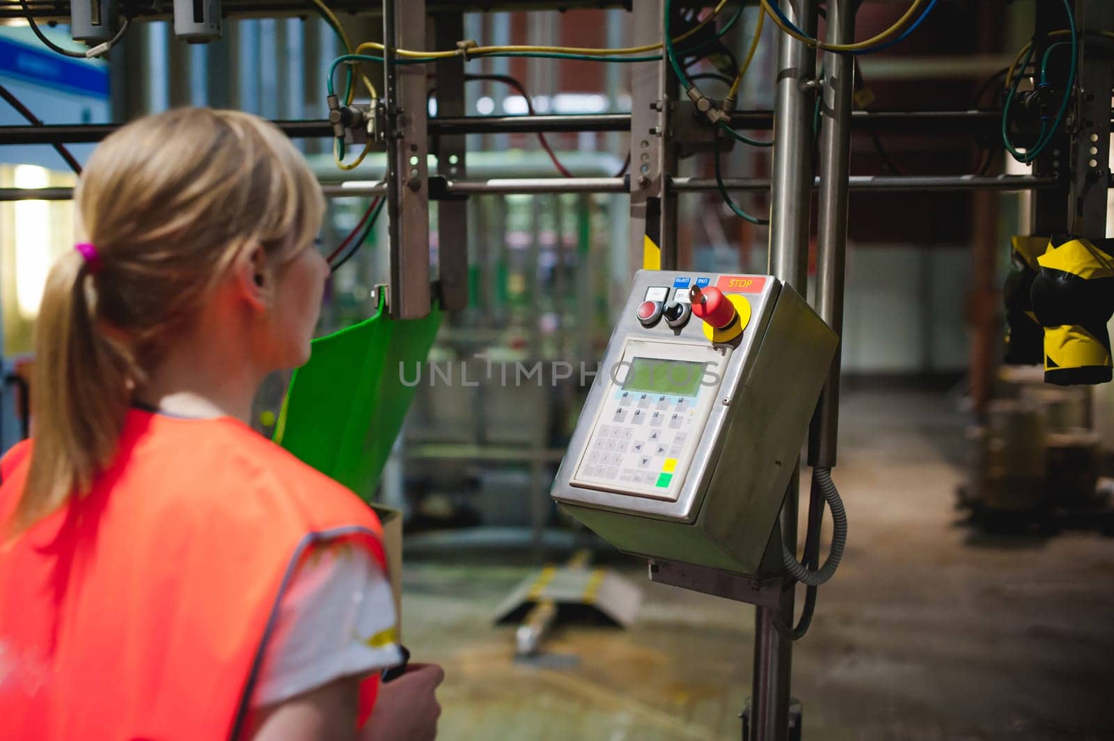 Portrait of a female employee in an orange robe vest in the working space of a production facility, supervises and controls the line in food production, against the background of equipment