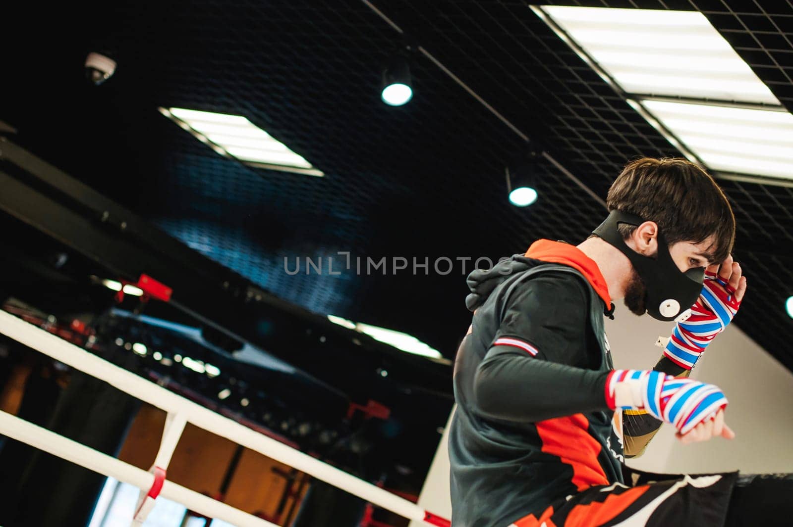 Professional Muay Thai fighter. Male boxer in training sportswear, an exercise in sports hall, fight with a shadow in ring, Strike testing in sports mask