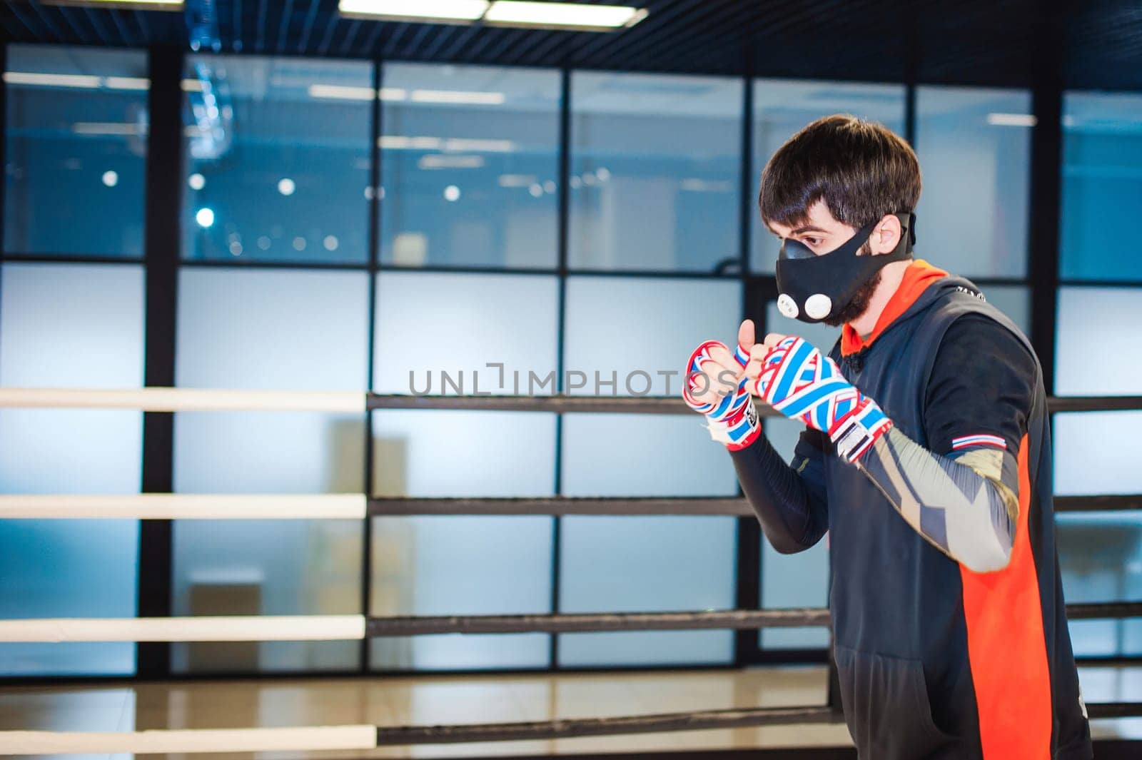 Professional Muay Thai fighter. Male boxer in training sportswear, an exercise in sports hall, fight with a shadow in ring, Strike testing in sports mask