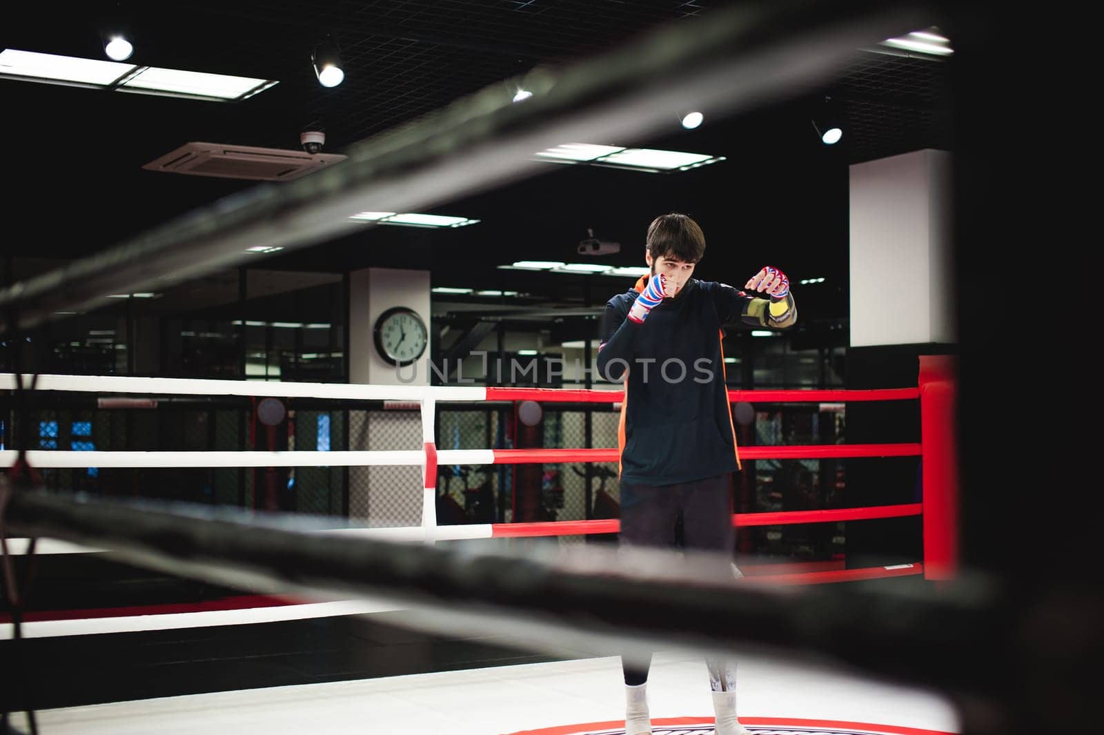 Professional Muay Thai fighter. Male boxer in training sportswear, an exercise in sports hall, fight with a shadow in ring, Strike testing