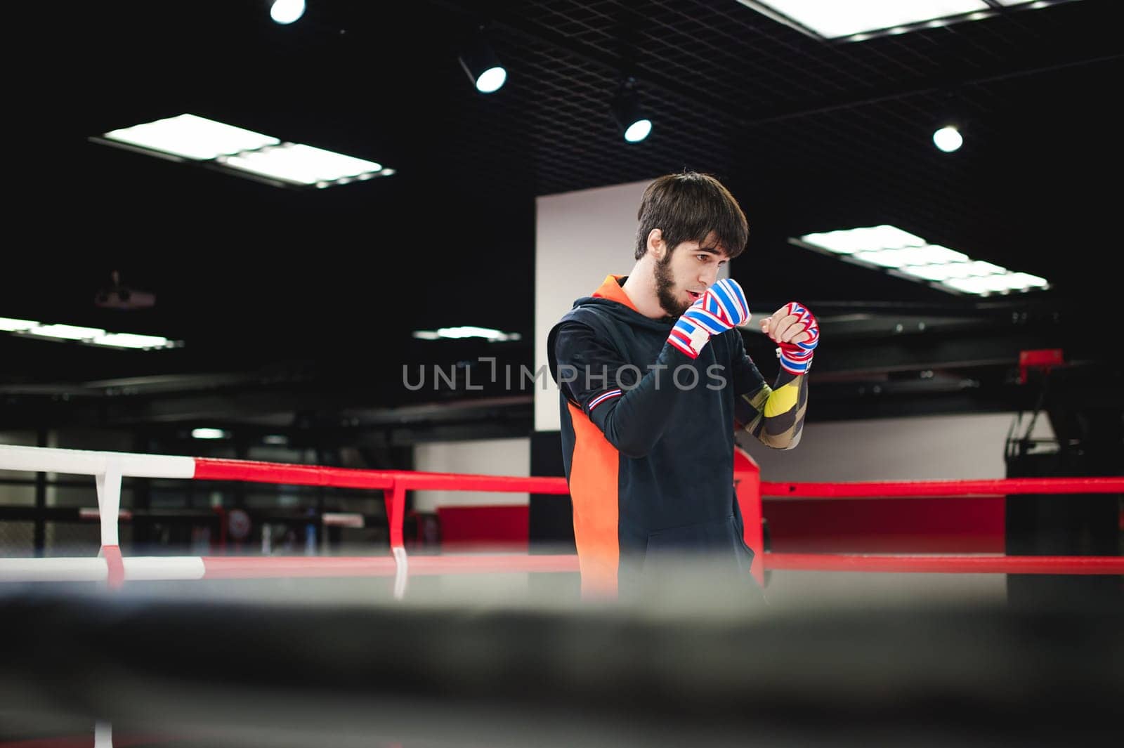 Professional Muay Thai fighter. Male boxer in training sportswear, an exercise in sports hall, fight with a shadow in ring, Strike testing