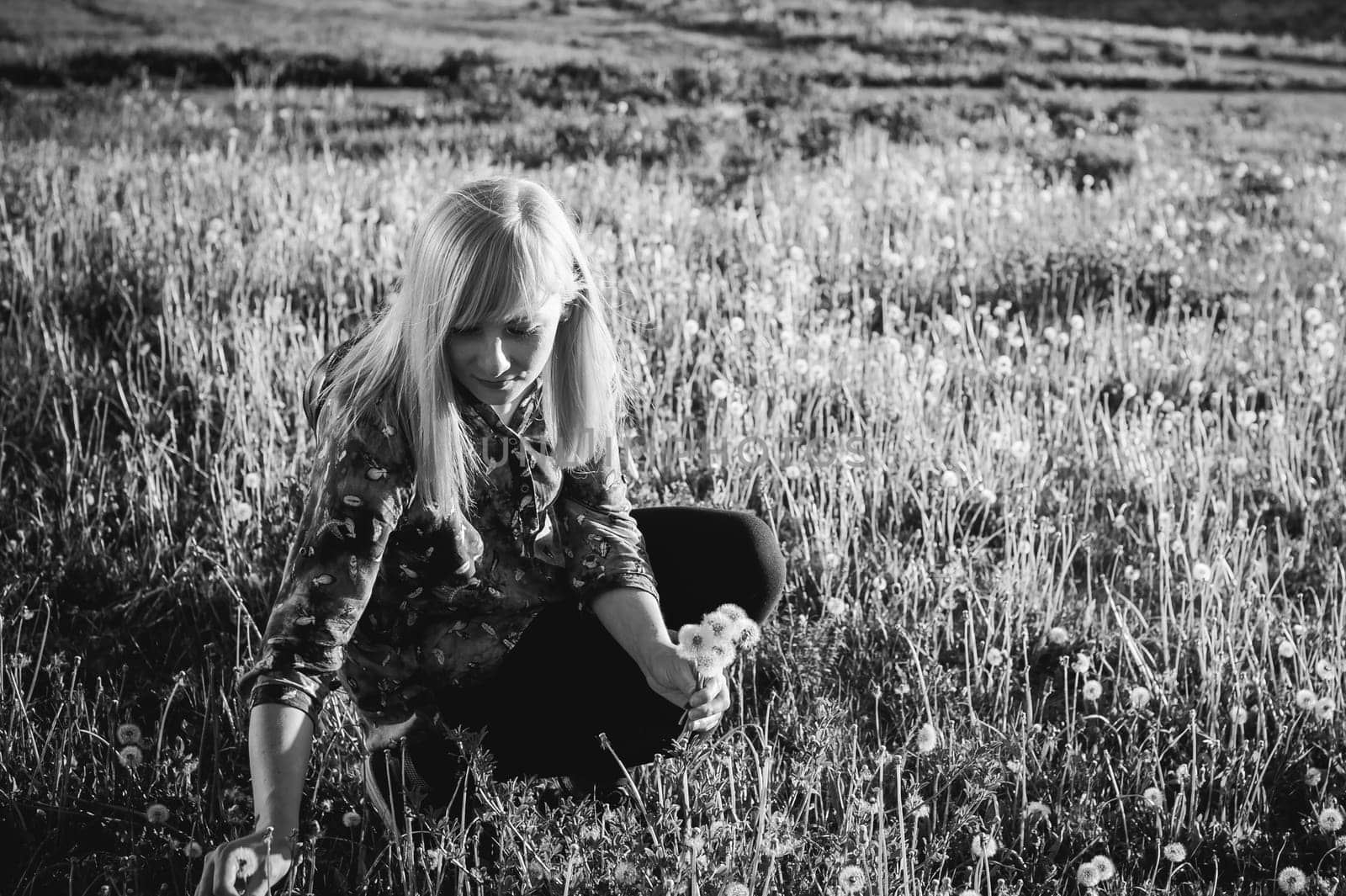 Young blonde girl in dress with shoulder bag, walking on dandelion field, against background of urban architecture, breathing relaxing in cityscape