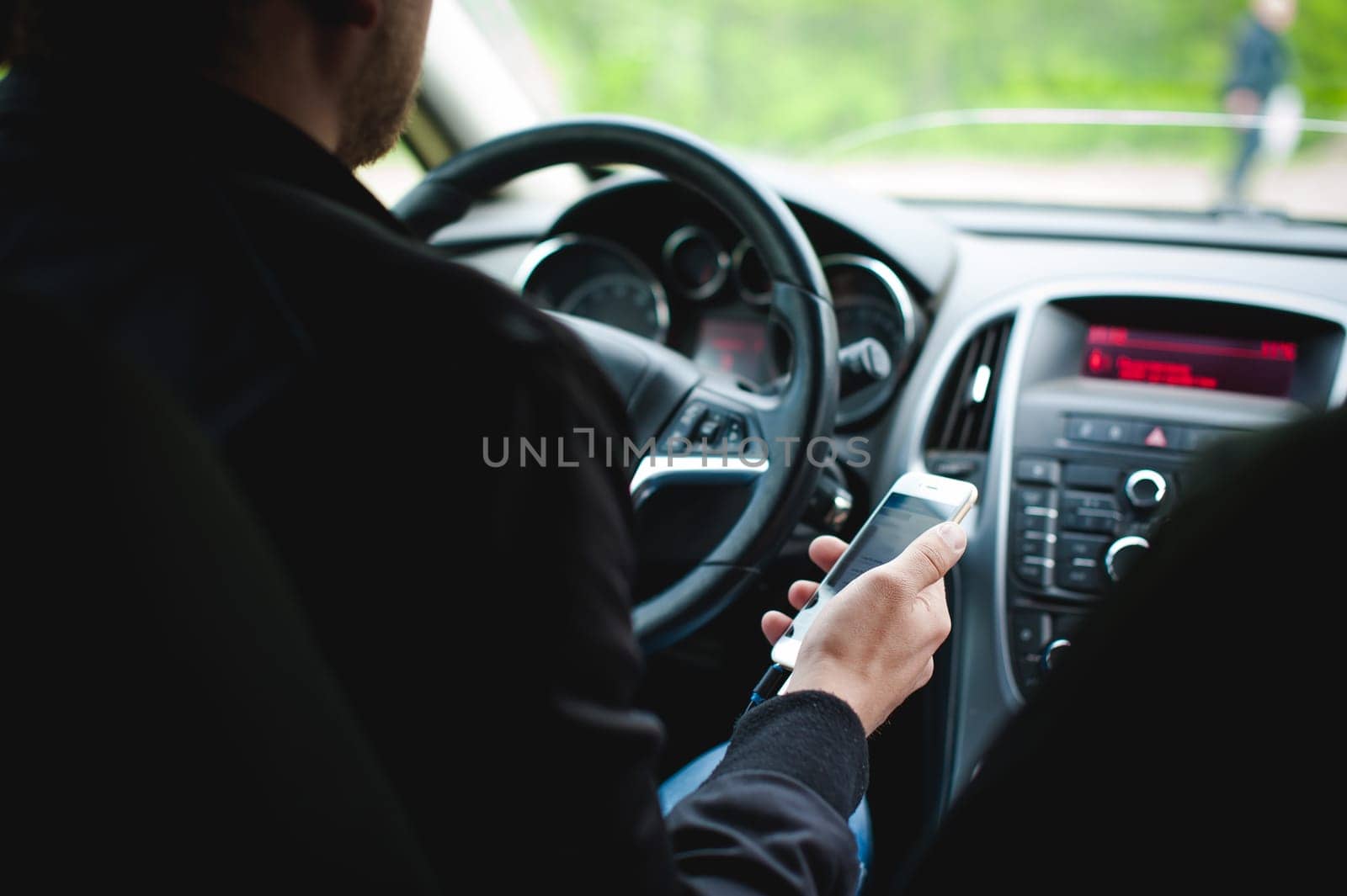 Man at the wheel of a car holds a phone in his hand