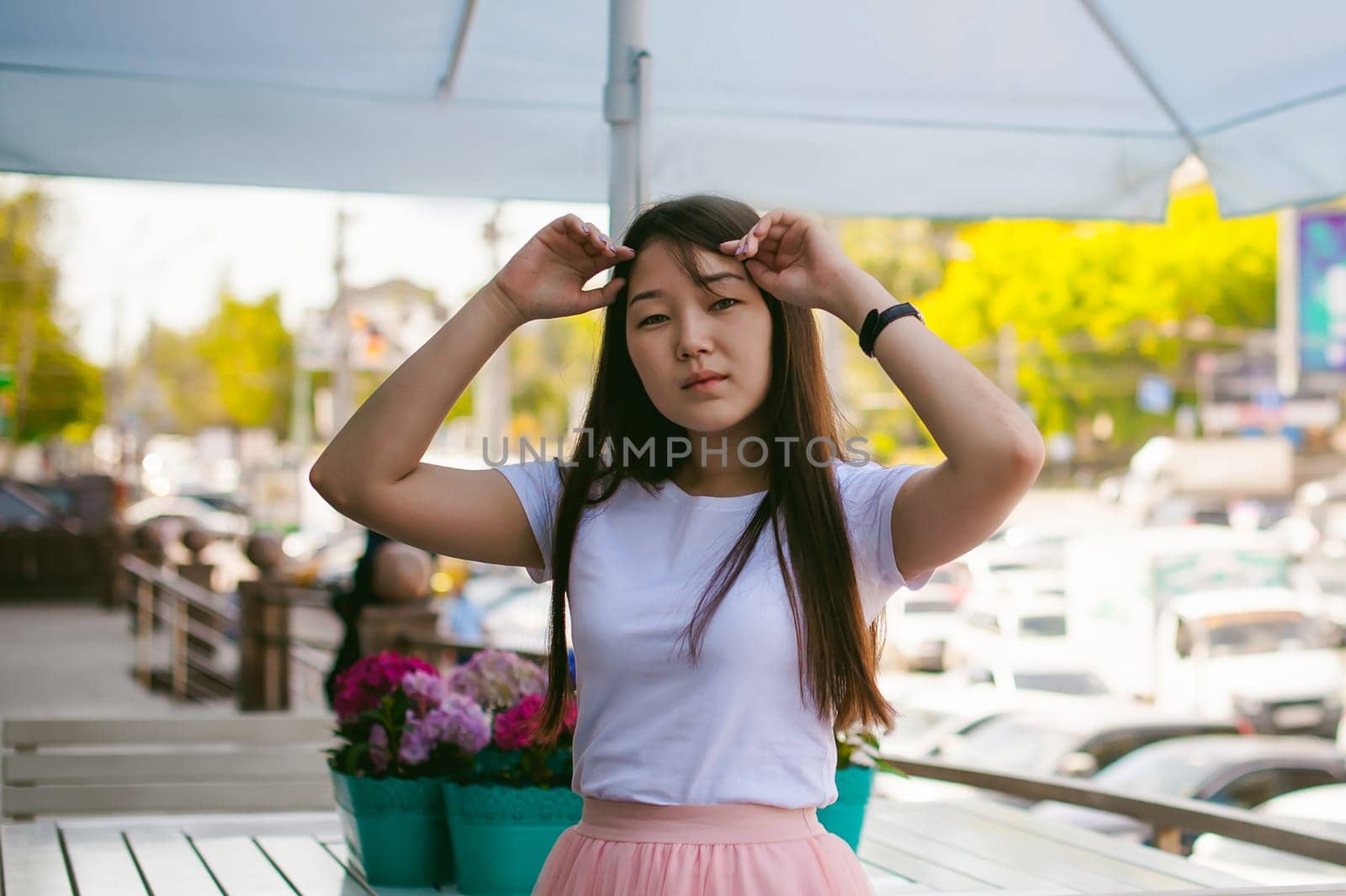 Cute asian young woman in summer cafe outdoors. girl In white T-shirt, with long hair in simple light cozy interior of restaurant Urban style