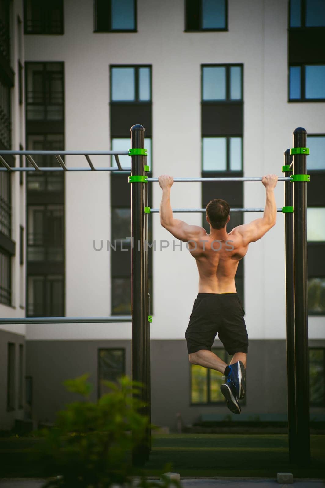 Handsome sexy male bodybuilder athlete man doing crossfit workout in athletic facilities on sunny morning outdoors. Healthy lifestyle concept. Physical preparation of body. pull-up on horizontal bar