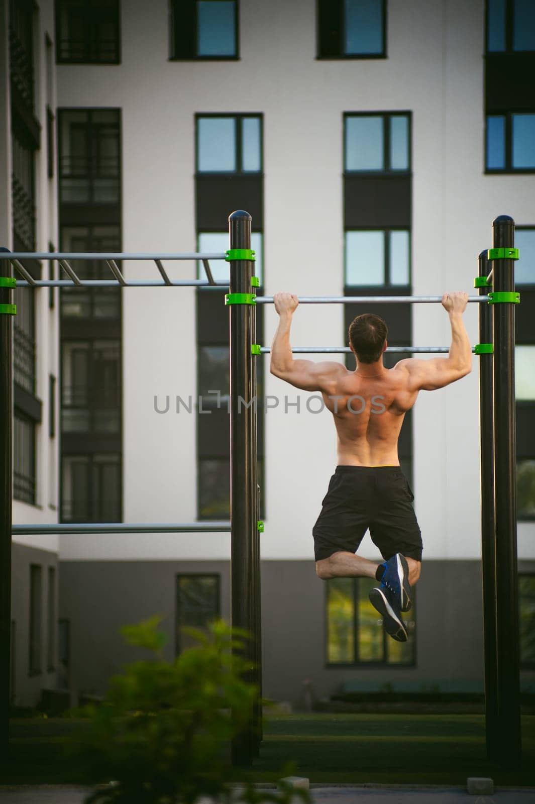 Handsome sexy male bodybuilder athlete man doing crossfit workout in athletic facilities on sunny morning outdoors. Healthy lifestyle concept. Physical preparation of body. pull-up on horizontal bar