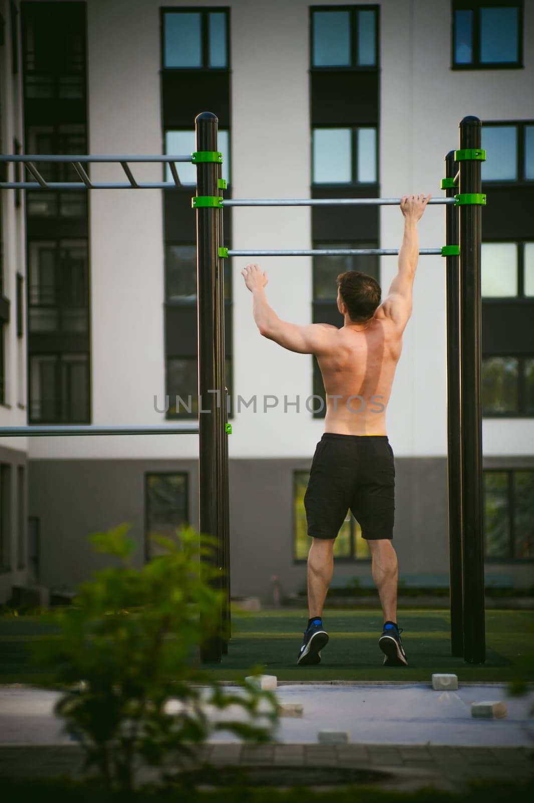 Handsome sexy male bodybuilder athlete man doing crossfit workout in athletic facilities on sunny morning outdoors. Healthy lifestyle concept. Physical preparation of body. pull-up on horizontal bar