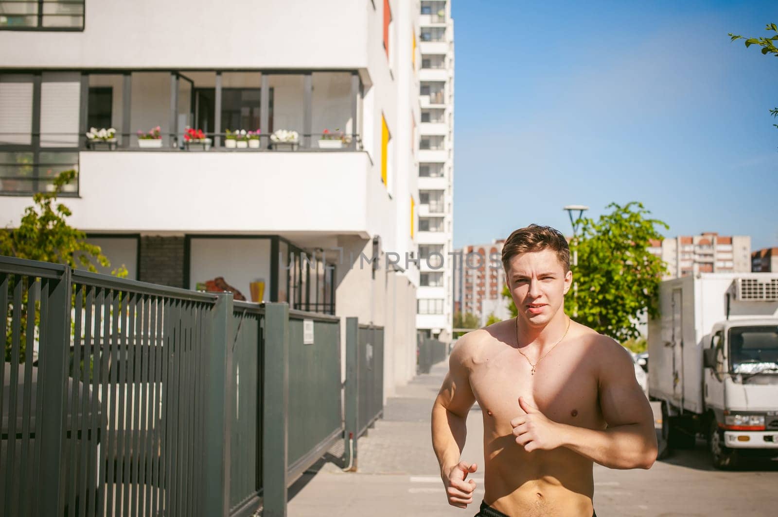Handsome sexy male bodybuilder athlete man with naked torso, Morning run in open air in urban courtyards, early sunny summer morning. Healthy lifestyle concept.