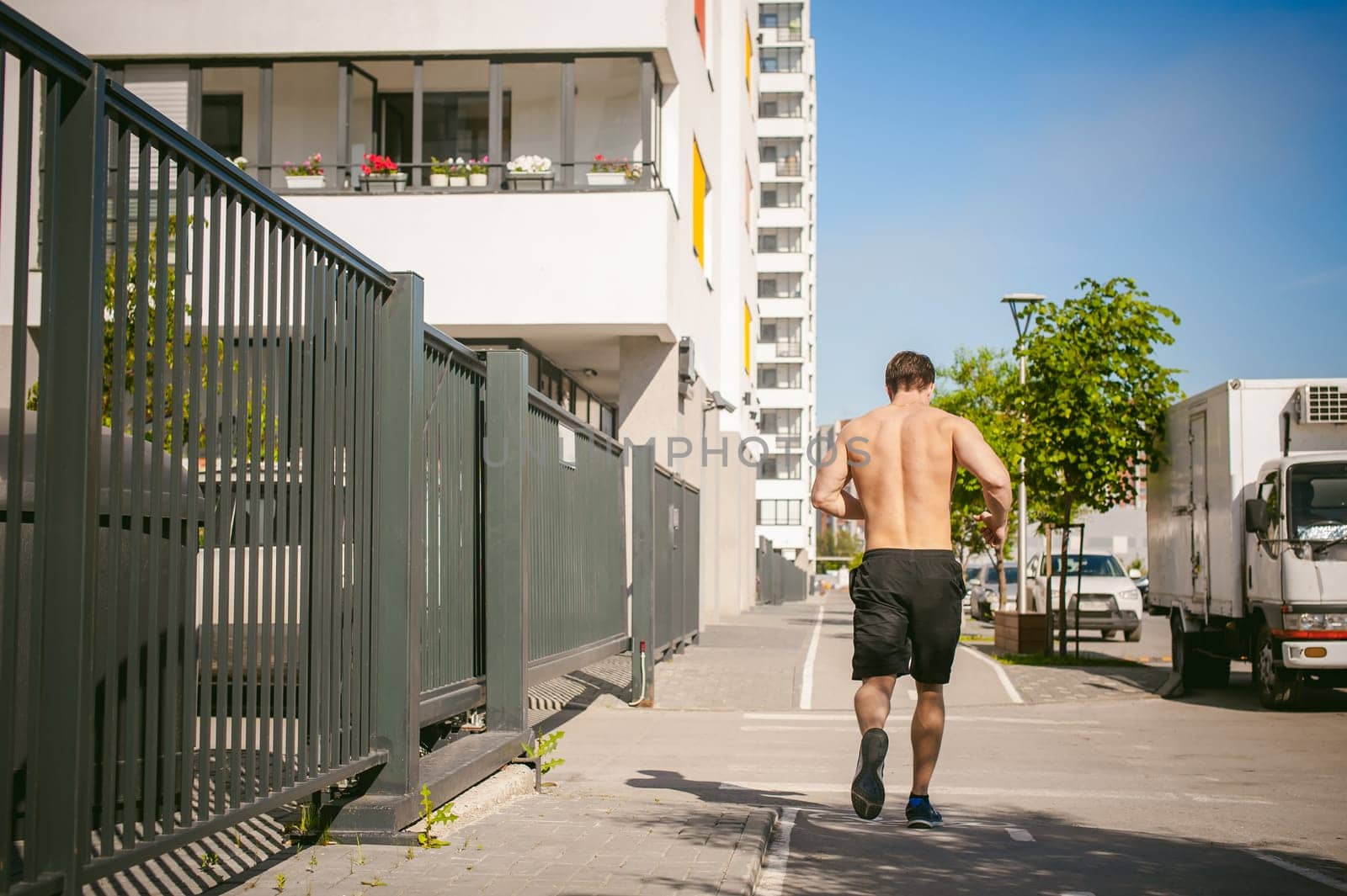 Handsome sexy male bodybuilder athlete man with naked torso, Morning run in open air in urban courtyards, early sunny summer morning. Healthy lifestyle concept.