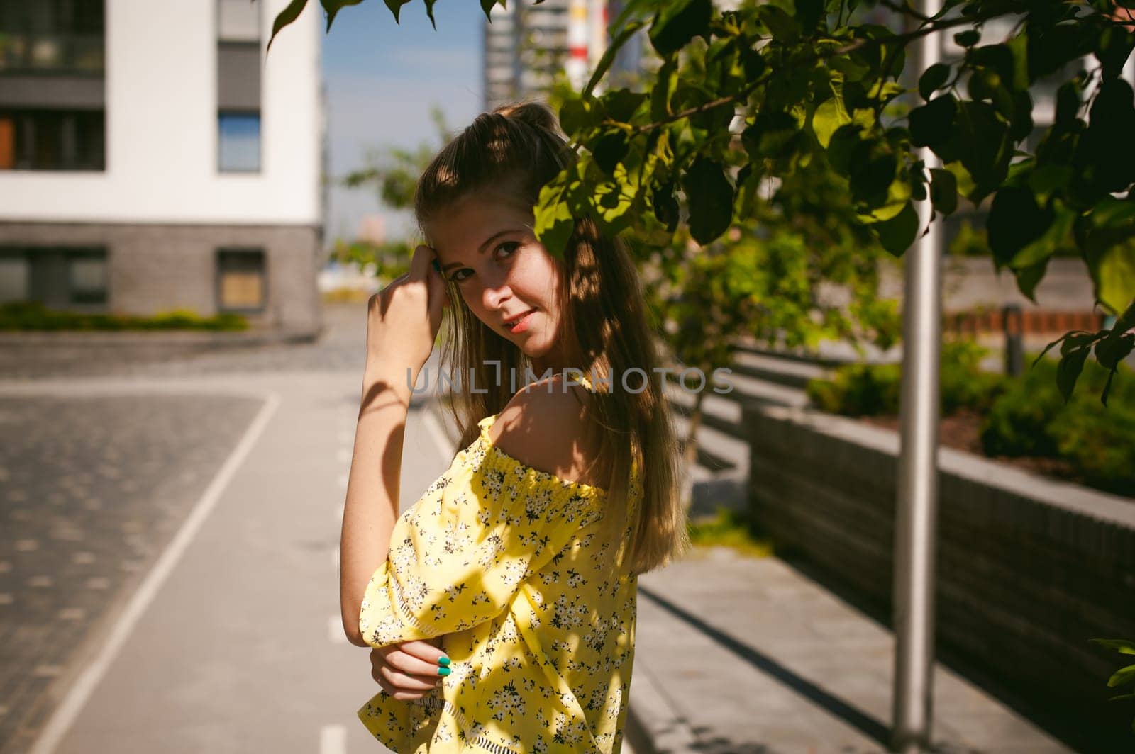 Young beautiful woman is strolling outdoors in the yard, against the backdrop of greenery and houses, warm summer sunny day